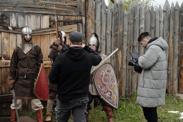 A behind-the-scenes photo of the 'The Witcher' Season 4 set, showing actors in costume and crew members preparing for a scene in a medieval-looking village.