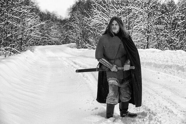 Liam Hemsworth as Geralt of Rivia, in full Witcher garb, sword drawn, facing an unseen enemy amidst a snowy landscape. The image attempts to mirror a classic Geralt pose to ease fan concerns.