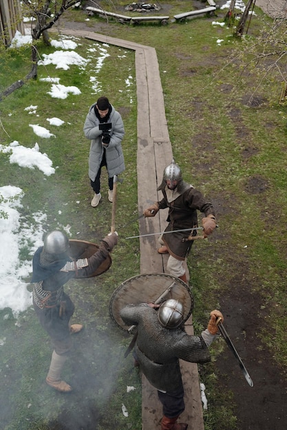 A group of Witcher trainees at Kaer Morhen, clad in training gear, practicing swordsmanship under the watchful eye of a senior Witcher. The scene captures the intensity and discipline of Wolf School training, with snow-capped mountains in the background.