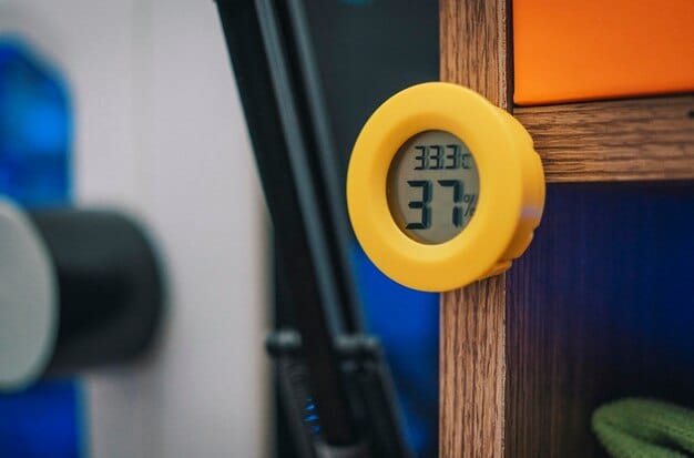 A close-up of a digital hygrometer displaying temperature and humidity readings in a comic book storage room. The comic books are visible in the background, stacked neatly in protective bags and boards.