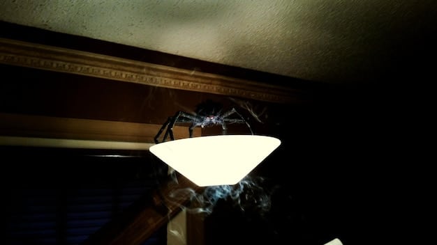 A photograph capturing the interior of a haunted house. Cobwebs hang from the ceiling, casting a dusty, eerie glow. Motion sensors can be seen in the corner with faint visible light.