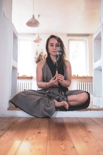A serene and softly lit space with a dark-haired woman meditating while sitting cross-legged on a cushion. In front of her is a black mirror, angled slightly upwards. The room is decorated with candles, crystals, and other spiritual items, creating a peaceful and focused atmosphere.