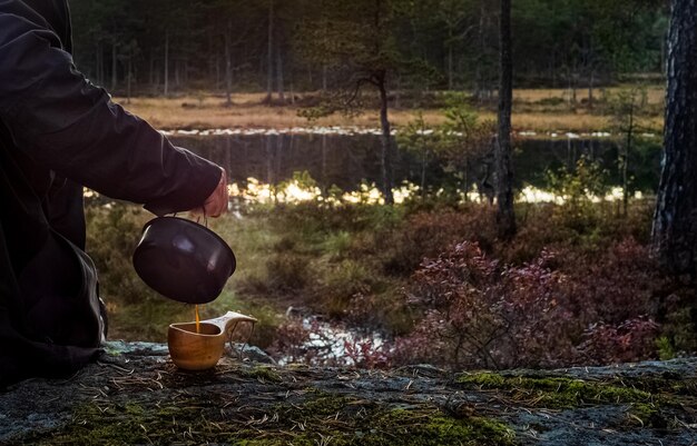 A witch stirring a bubbling cauldron over an open fire in a dimly lit forest clearing. She is dressed in flowing robes and wears a pointed hat, her face illuminated by the firelight. Various herbs and tools are scattered around her workstation.