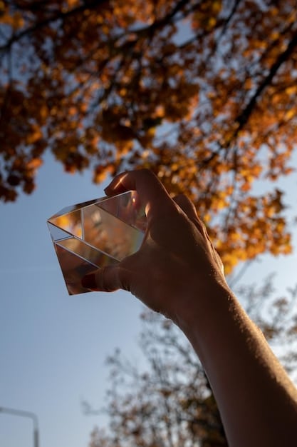 A close-up shot of a hand holding a clear quartz crystal, with a blurred background of various other crystals and meditation candles.