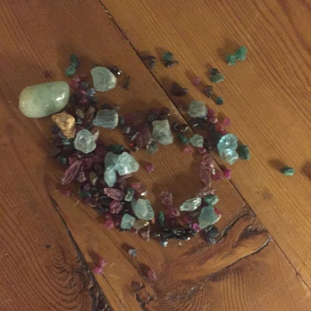 An overhead shot of various crystals laid out on a wooden surface. Included are amethyst, rose quartz, clear quartz, and labradorite. Each crystal is clearly labeled with a small tag, and there is a measuring tape present to indicate size. The image emphasizes the diversity of crystals and their distinct appearances.