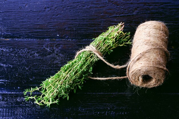 A close-up of vibrant green Rosemary sprigs, bundled together with twine, resting on a rustic wooden table amidst scattered dried rose petals and a worn, leather-bound Book of Shadows, symbolizing Rosemary's protective and memory-enhancing properties within witchcraft.