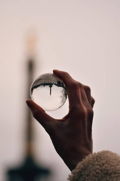A close-up of hands gently holding a clear crystal ball. The crystal ball reflects the surrounding environment, creating a distorted and ethereal view of the room. The focus is on the crystal ball and the hands that cradle it, emphasizing the connection between the practitioner and the divination tool.