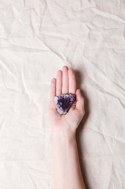 A close-up shot of a person's hand holding a polished amethyst crystal. The background is blurred, but suggests a peaceful, natural setting like a garden. The focus is on the deep purple color and smooth texture of the amethyst, emphasizing its role in Crystal Healing for Beginners: A Step-by-Step Guide to Cleansing and Charging Your Crystals.