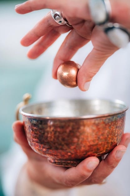 A close-up shot of a crystal being held near a singing bowl. The bowl is vibrating, and the crystal is positioned to receive the sound waves. The background is soft and out of focus, highlighting the interaction between the crystal and the sound.